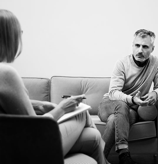Duas pessoas conversando, uma de costas e uma de frente preocupada, sentada no sofá